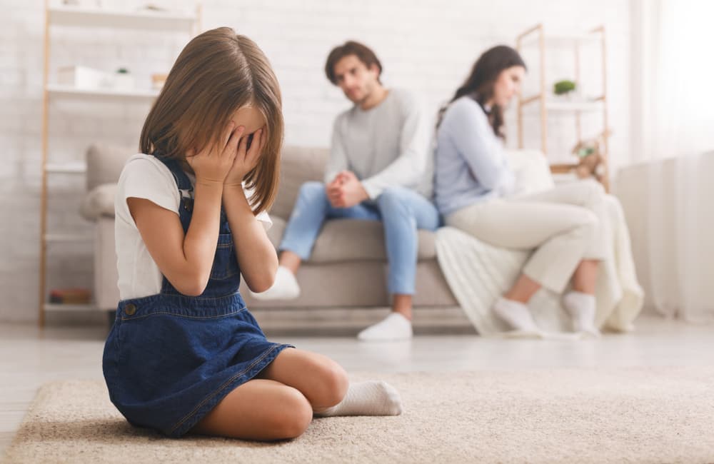 A crying little girl sits apart from her parents after their argument, feeling upset and lonely, exhausted by the constant quarrels.