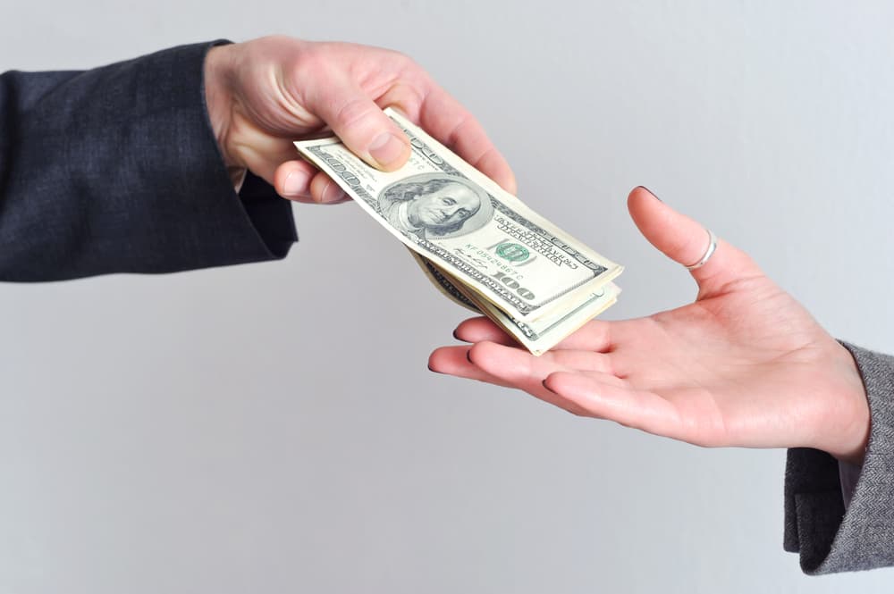 A man's hand extending cash towards a woman's hand, which reaches out to receive the money.






