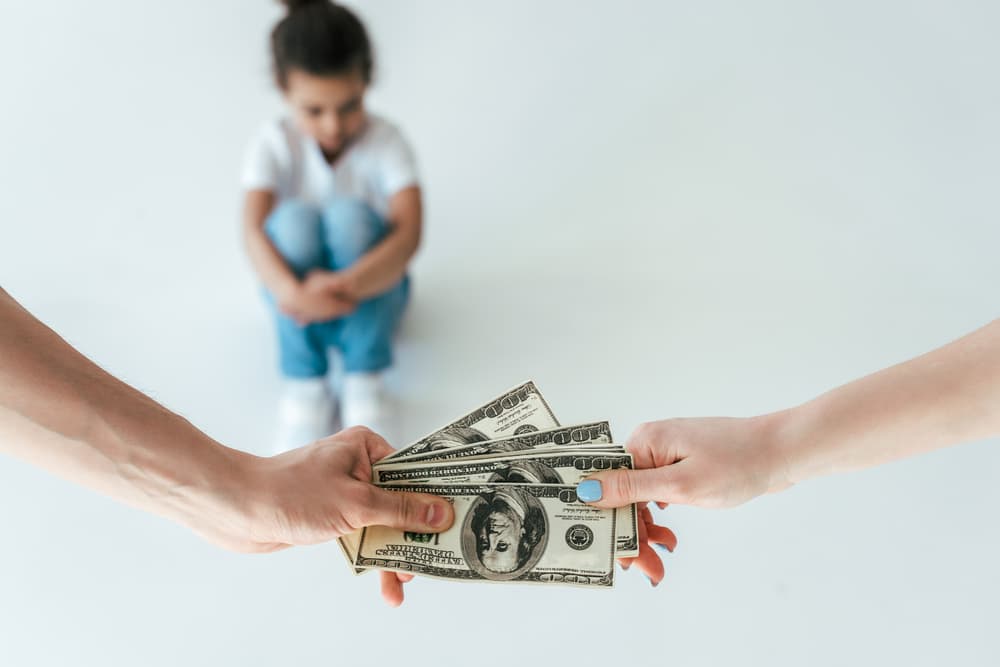 A selective focus image showing a man handing alimony to a woman, with their child nearby. The emphasis is on the exchange, symbolizing spousal support after a divorce, while the child, slightly blurred in the background.