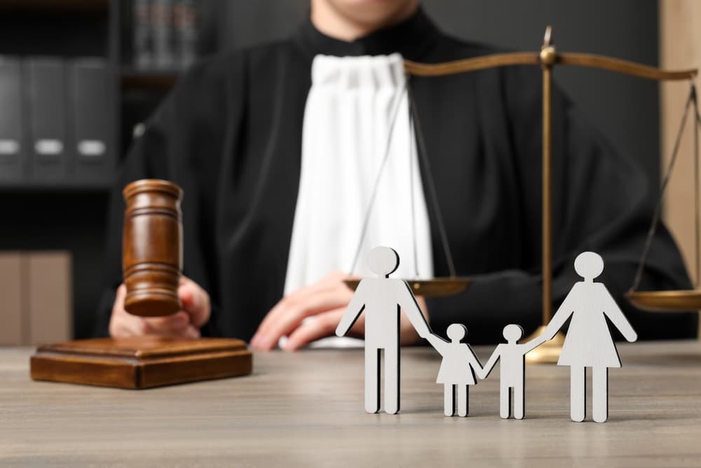 A family law judge, holding a gavel and surrounded by scales of justice, sits at a wooden table. 