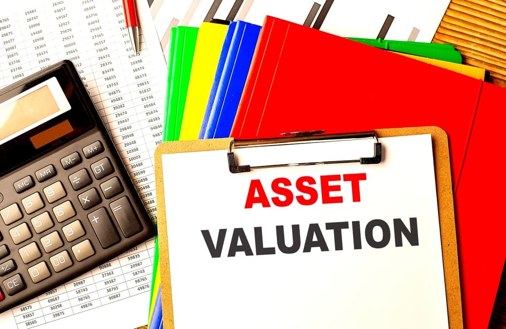 ASSET VALUATION text on a clipboard with calculator and color folder .