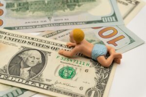 Miniature baby toys on the table with dollar bills.